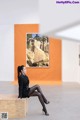 A woman sitting on a bench in front of a painting.