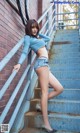 A woman in a blue top and denim shorts posing on some stairs.