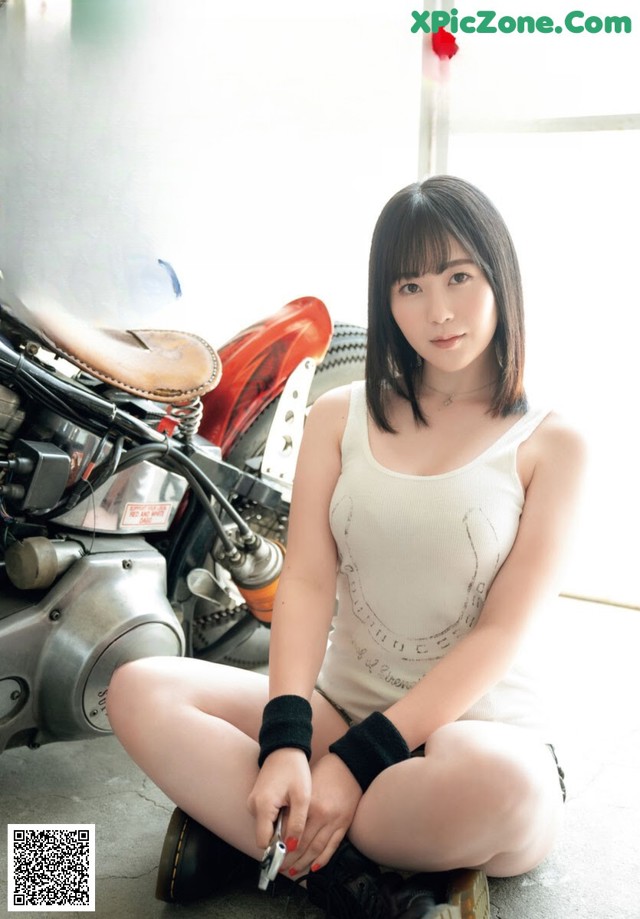 A woman sitting on the ground next to a motorcycle.
