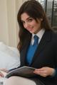 A woman in a business suit sitting on a bed reading a book.